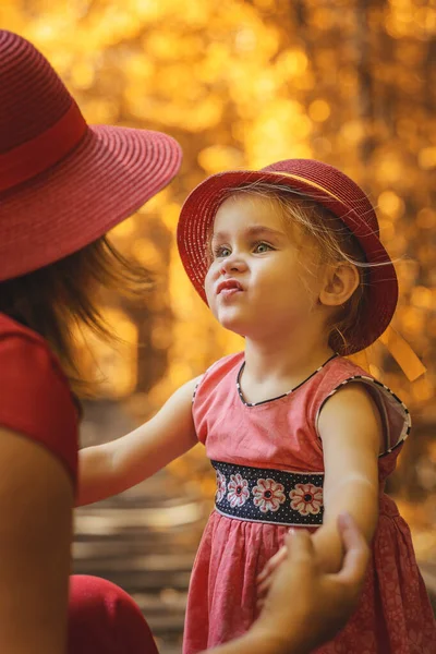 Mamá con hija en sombreros rojos caminando en otoño en túnel de amor . —  Fotos de Stock