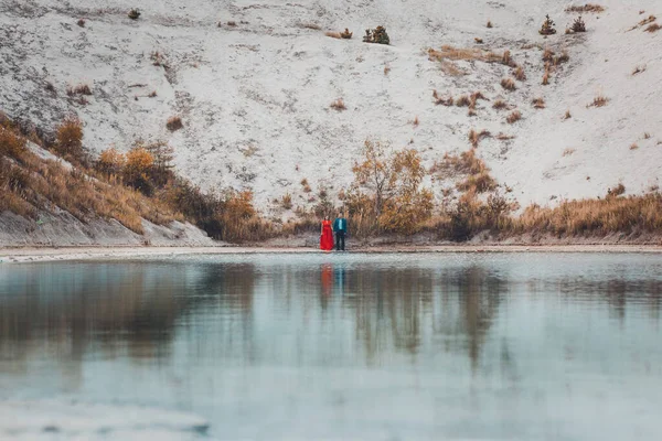 Όμορφο ζευγάρι με τα πόδια στα φωσφορικά-γύψο λευκά βουνά της Ουκρανίας, το κορίτσι σε ένα κόκκινο φόρεμα σε ένα φόντο μιας πράσινης λίμνης. — Φωτογραφία Αρχείου