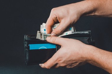 Adamın eli cüzdan, siyah arka plan ve siyah cüzdandan para çekiyor.