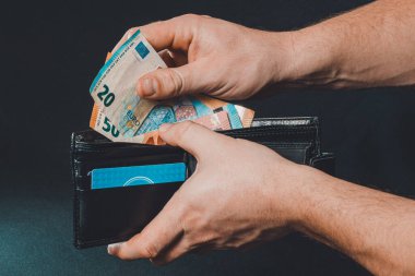 İnsan ellerine yakın çekim. Siyah arka planda izole edilmiş bir cüzdana avro banknotları koyuyoruz. 2020