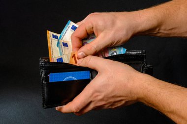 İnsan ellerine yakın çekim. Siyah arka planda izole edilmiş bir cüzdana avro banknotları koyuyoruz. 2020