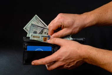 Siyah arka plandaki adam elinde dolarlarla dolu bir cüzdan tutuyor.