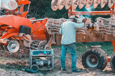 The farmer repairs the harrows if they are damaged by hitting stones. A master welder welds metal parts of agricultural equipment 2021. Ivano-Frankivsk region clipart
