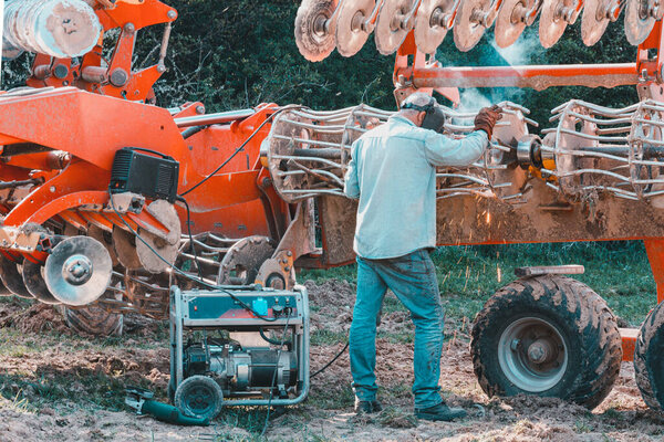 The farmer repairs the harrows if they are damaged by hitting stones. A master welder welds metal parts of agricultural equipment 2021. Ivano-Frankivsk region