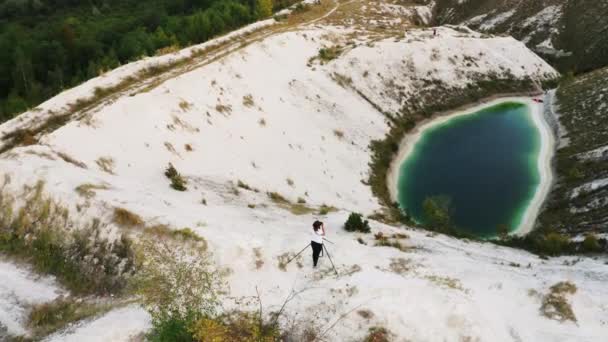 Ο φωτογράφος τοπίων με μια κάμερα σε ένα τρίποδο φωτογραφίζει μια πράσινη τεχνητή λίμνη στα λευκά βουνά. Φωσφόρος-γύψος σωρούς. Αεροφωτογραφία 4k — Αρχείο Βίντεο