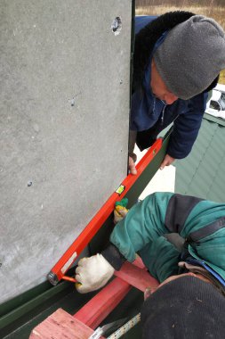 İşçiler bacayı yeşil metalle kaplıyorlar, sigortalı değiller, seviye, mezura ve ahşap iskele kullanıyorlar..