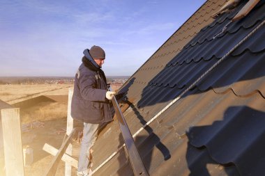 The master works on the roof of a private house without insurance, the work is performed in the cold season, the worker behaves carefully, the roof is green.2020 clipart