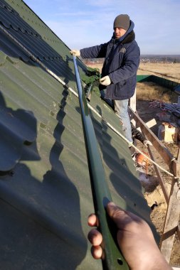 Usta, sigorta elementleri, yeşil çatı ve metal fayansların olmadığı bir çatıda çalışıyor. Kırsal kesimde özel bir ev..