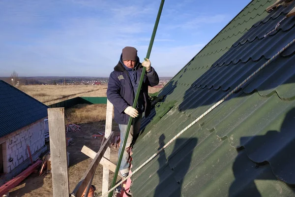 The master works on the roof of a private house without insurance, the work is performed in the cold season, the worker behaves carefully, the roof is green.2020