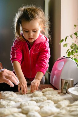 Büyükannem ve torunum et dolu hamur köfteleri yontuyorlar. Masanın üzerinde un, dolma, kıyma makinesi ve mutlu bir büyükanne ve torun var. 2020.