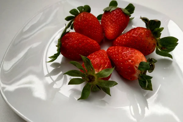 Reife Erdbeeren auf einem Teller, ein weißer Teller, eine Beere in Nahaufnahme, saftige und reife Erdbeeren mit grünen Blättern. — Stockfoto