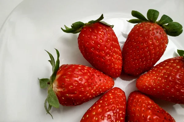 Fresas maduras dispuestas en un plato, un plato blanco, un primer plano de bayas, fresas jugosas y maduras con hojas verdes. — Foto de Stock