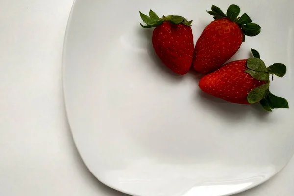 Frische hausgemachte Erdbeeren auf einem Teller mit weißem Porzellan, drei saftige Erdbeeren auf einem Teller, glänzend weißer Teller. — Stockfoto