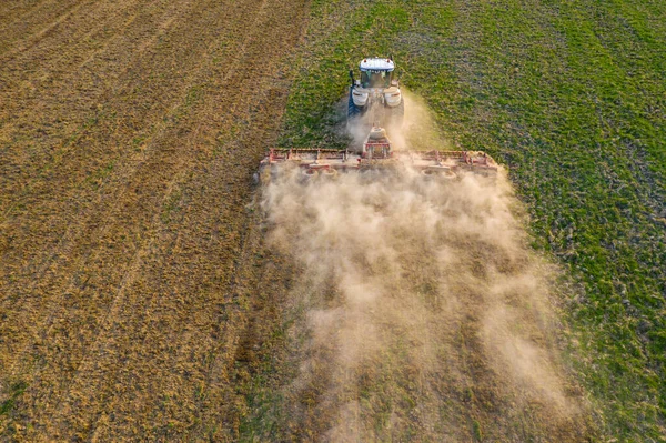 Large agricultural machinery works on Ukrainian fields, cultivation of Carpathian fields before sowing of grain crops, fields are located near the forest.2021