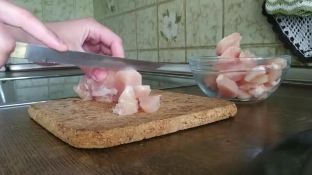 Jovem mulher corta filé de frango na cozinha com uma faca de cozinha. Cozinhar pratos de carne em casa . — Vídeo de Stock
