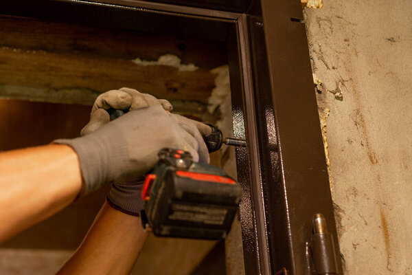 The master drills holes with a hand drill in a metal door box, close-up, installation of new doors.2020