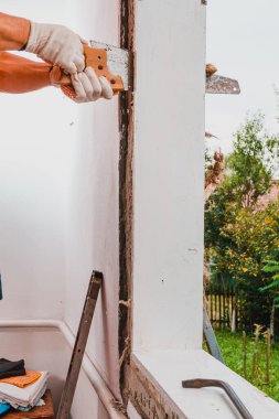 Eli testereli adam pencere çerçevesinin etrafındaki montaj yününü kesiyor, eski ahşap bir pencerenin montajı, pencere yenilenmesi. 2020