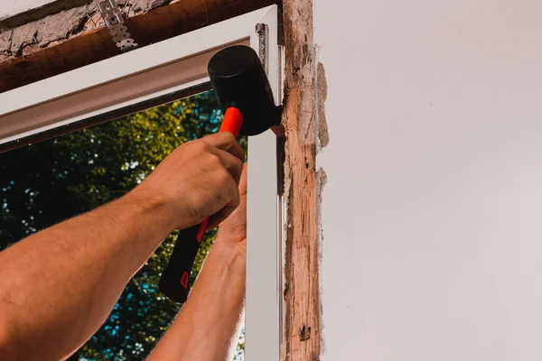 Window installation, a new plastic window in a private house, the master uses a rubber hammer to install the window.