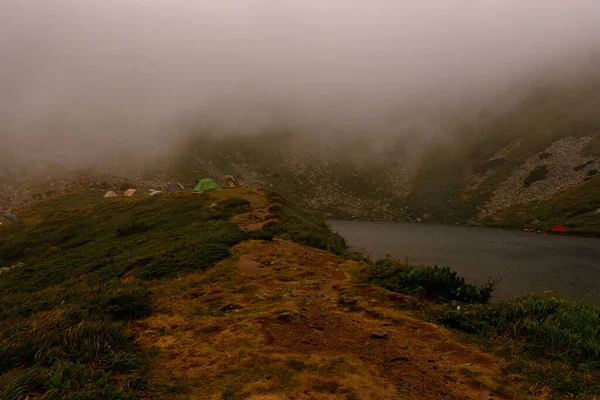 Mountain lake, tourists near a mountain lake, rain in the mountains, tourists in raincoats, fog near the lake in the Carpathians, the highest lake in the Carpathians of Ukraine Brebeneskul.2020