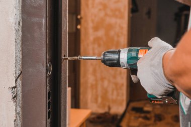 Marangoz duvarda ve metal kapı çerçevesinde matkapla delikler açar, daha sonra vidaları vidalar ve kapı çerçevesini 20.20 'ye bağlar.
