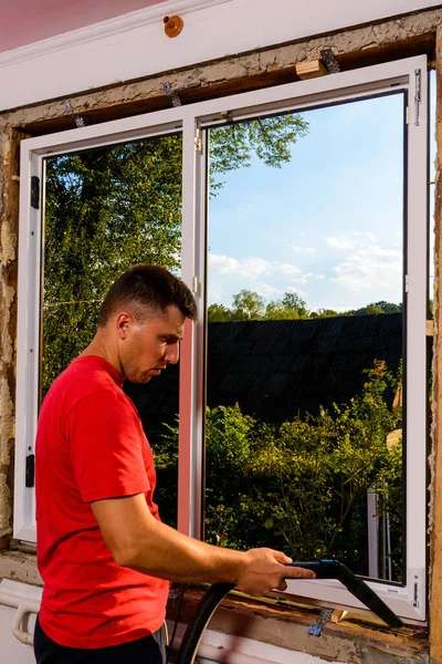 男は泡で窓のさらなる断熱のための分解と組立のほこりや破片の後に余分な左を削除するために掃除機を使用しています 2020 — ストック写真