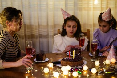 Üç arkadaş, pasta, köpüklü içeceklerle dolu keyifli bir akşamı paylaşıyor ve neşeli şapkalar takıp birlikte gülüyorlar, birlikte anılar yaratıyorlar..