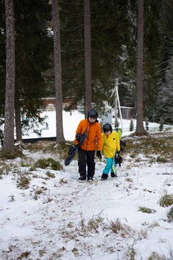 Kış kıyafetleri içinde giyinmiş iki birey, karla kaplı bir yolda, yüksek çam ağaçlarıyla çevrelenmiş, sakin bir arazide kayak macerasının heyecanını kucaklıyor..