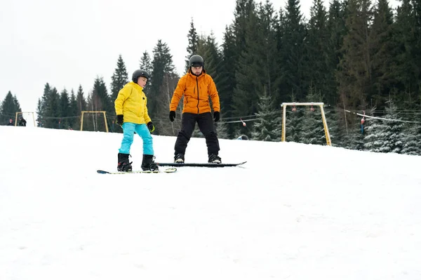 Bir çocuk karda dikkatlice süzülürken heyecan ve neşe, sakin bir kış manzarası ve uzun ağaçlar arasında yetenekli bir eğitmenden rehberlik alırken..