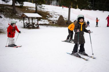 Çocuklar hevesle kayak kursunda geziniyor, yeteneklerini ustalıkla, neşeyle dolu, pitoresk bir kış manzarasında eğitmenlerin dikkatli bakışları altında öğreniyorlar..