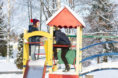 İki çocuk renkli bir oyun bahçesinde oynayarak karlı bir kış gününün tadını çıkarıyor. Yapı kısmen karla kaplı, kış harikalar diyarına ekleniyor..