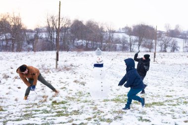Üç arkadaş karlı bir günün tadını çıkarıyorlar. Kardan adam yapıp kartopu atıyorlar. Sahne, arka planda ağaçlar ve hafif bir kar tozu olan kırsal bir arazide geçiyor..