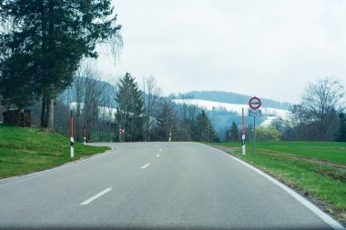 Huzurlu bir yol boyunca kıvrılarak, yemyeşil her iki tarafı da sarar. Nazik tepeler arka planda yükselirken, bulutlu gökyüzünün altında macera ve barış vaat eder..