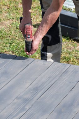 Sanatçı, çardağın tabanını sağlamlaştıran vidaları sıkılaştırmak için bir tornavida kullanıyor..