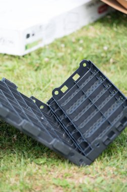 Koyu gri bir plastiğin yeşil çimlerin üzerinde uzanan yakın çekimi. Modüler ve muhtemelen daha büyük bir montajın parçası. Arka plan biraz bulanık..