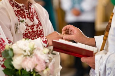 Bir düğün töreninin yakın çekimi. Görevli gelinin ya da damadın parmağına yüzük takar. Bir buket çiçek görünüyor..