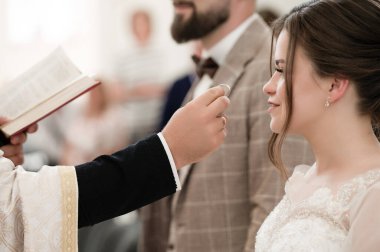 Resmi bir düğün seremonisi yakalandı. Nikah memuru, çiftler birliğinin bir sembolü olan yüzükleri sunar. Gelinin beklentisine ve anın kutsallığına odaklan..
