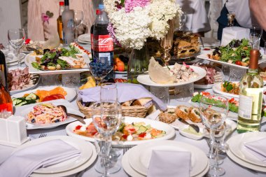 Aperatifler, salatalar ve başlangıç yemekleriyle dolu bir masa. Tabakları kaplayan bardaklar ve şişeler şenlikli bir atmosfer yaratıyor..