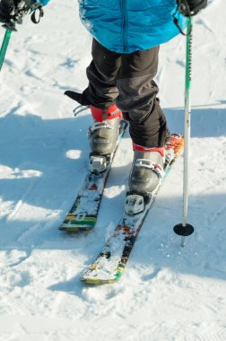 Odaklanmış kayakçı karlı bir yamaçta duruyor, dağdan aşağı süzülüyor, renkli kıyafetler giyiyor ve kış sporları için azim ve heyecanla kayak direklerini kavrıyor..