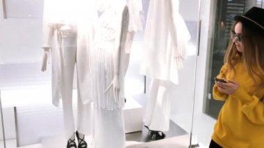 Genç esmer kız online alışveriş. Kız Giysi dükkanında seçer ve telefon üzerinden online satın almak. Kız sarı kazaklı, şapka satın telefon uygulaması ile. 