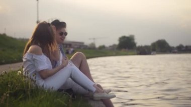 Trandy iki nehir kenarında konuşuyor. Tatil, tatil, sevgi ve insan kavramı - mutlu genç çift yaz Visla nehir kenarında oturan. Lought kalma, konuşan çift. Eğlence Parkı arka plan, dönme dolap