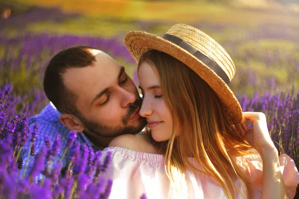Cute young couple in love in a field of lavender flowers.  Enjoy a moment of happiness and love in a lavender field. Boy kiss his girl. Blond girl in hat. Romantic couple.