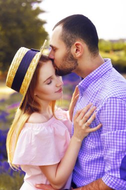 Sevimli genç mutlu çift bir alanda aşık lavanta çiçek. Mutluluk ve sevgi bir lavanta alandaki bir anın tadını çıkarın. Çocuk kızı öp. Şapkalı sarışın kız. Romantik Çift.