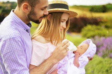 Beyaz aile anne, baba ve kızı mutlu giyen beyaz giysiler lavanta alanında eğlenceli yaşıyorsanız. Bir çift bir bebek bir şişe, Bebek süt besleniyor. Aşk, Genç çift.