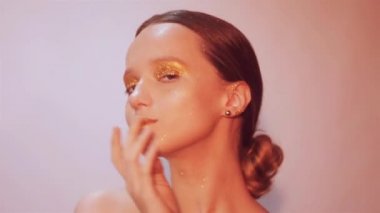 Zarif kız genç moda. Paslet arka plan, stüdyo. Altın dudaklar ve altın parlak makyaj güzel esmer kadın. Ve kadın ile şık saç olun. Poz ve parlayan, closeup saxy kız. 60fps