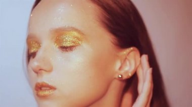 Zarif kız genç moda. Paslet arka plan, stüdyo. Altın dudaklar ve altın parlak makyaj güzel esmer kadın. Ve kadın ile şık saç olun. Poz ve parlayan, closeup saxy kız. 60fps