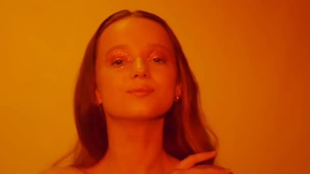 ファッション エレガントな少女 Paslet スタジオ ゴールドの唇と黄金の明るいメイクで美しいブルネットの女性 スタイリッシュな髪を持つ女性 Saxy 女の子ポーズと 赤いネオンに輝きます Fps — ストック動画