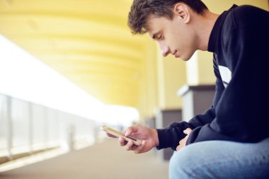 Tren istasyonunda seyahat onun akıllı telefon uygulama kullanan adam. Tren istasyonunda yakışıklı. Serbest adam gülümse. Çocuk ile bir telefon tutarak ve bir tren istasyonunda bekleyen sırt çantası