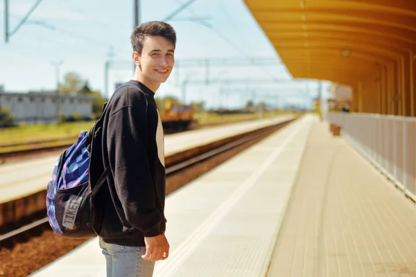 Man on train station, travel. Student in railway station. Smile freelance man. Boy with backpack waiting in a train station in sunny day smile.