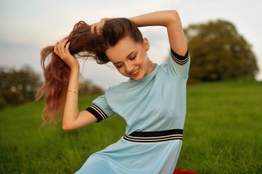 Onun zaman dışında günbatımı park zevk çekici genç kadın. Muhteşem uzun saçları açık poz ile modeli kız. Güzellik, moda kavramı. Mavi elbiseli güzel bir esmer portresi.