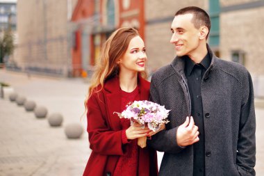 Genç romantik çift, şehirde kalma çiçekler ile güzel kız var. Gri paltolu ve model kırmızı paltolu adam. Mutlu sevgi dolu, gülümseme, bir yürüyüş birlikte Alışveriş Merkezi yakınındaki bir authmn günü zevk.. 